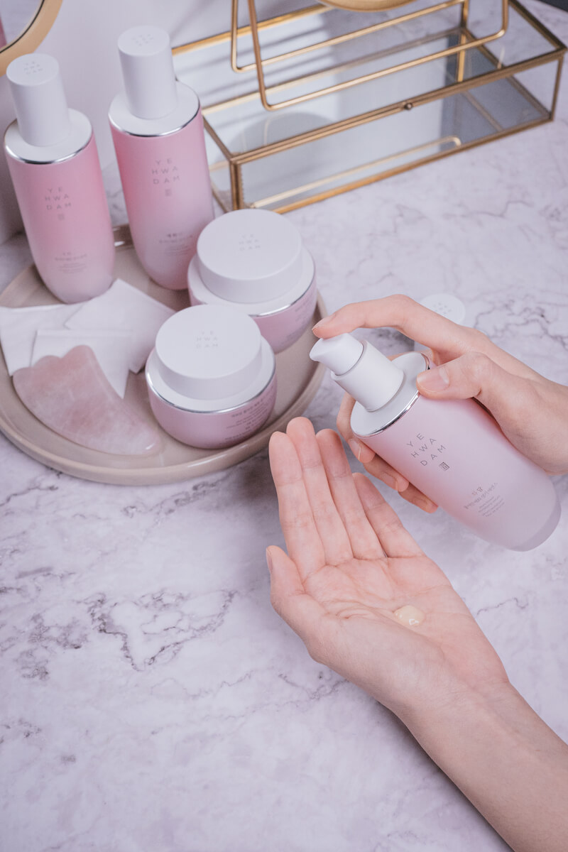 A hand applying pink skincare products on marble background